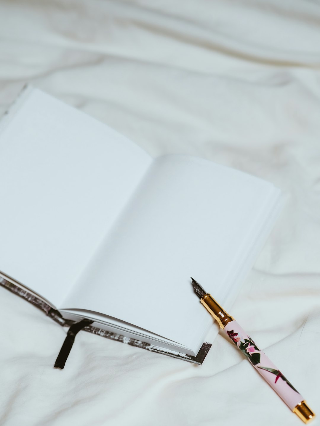 A notebook and floral fountain pen on a bed.